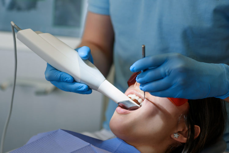 Close up dentist's hands scans the patient's teeth with a 3d scanner. 